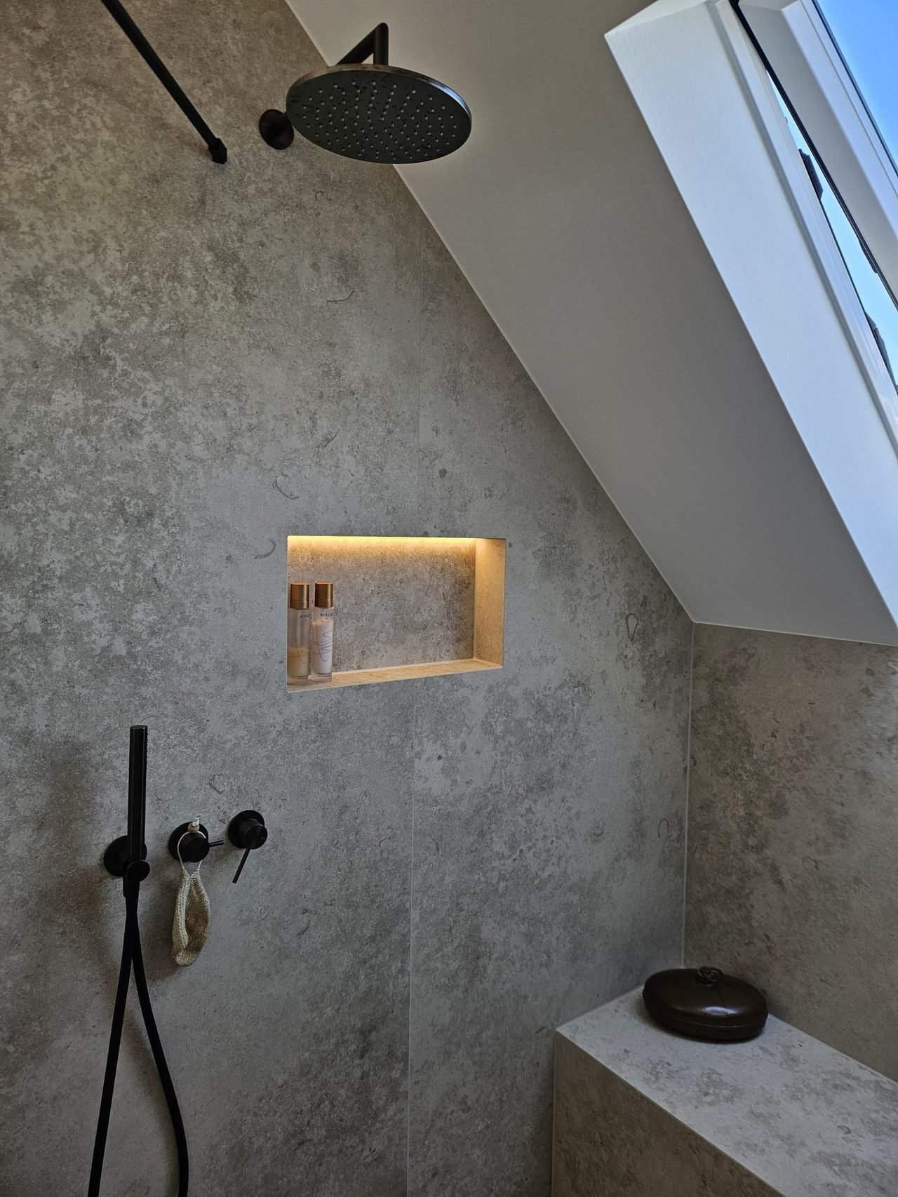 Bad in Betonoptik mit schwarzen Akzenten – Regenbrause und Dachflächenfenster – Atmosphäre im Duschbereich